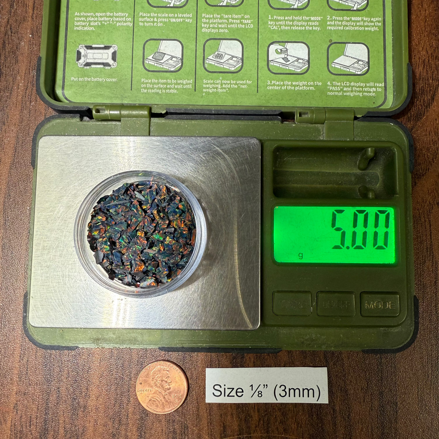 5-gram container of material on a wooden surface, showing a weight reading.