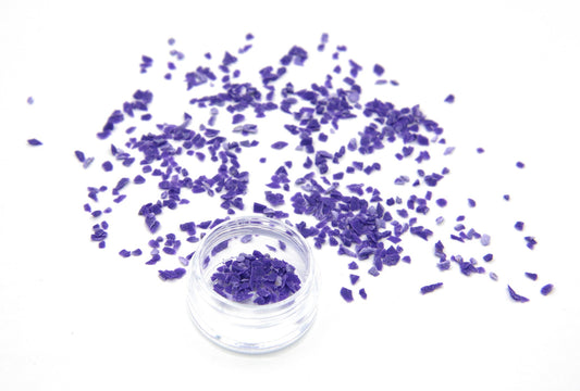 Purple Colorstone fragments scattered on white, with a small jar of the crushed stone