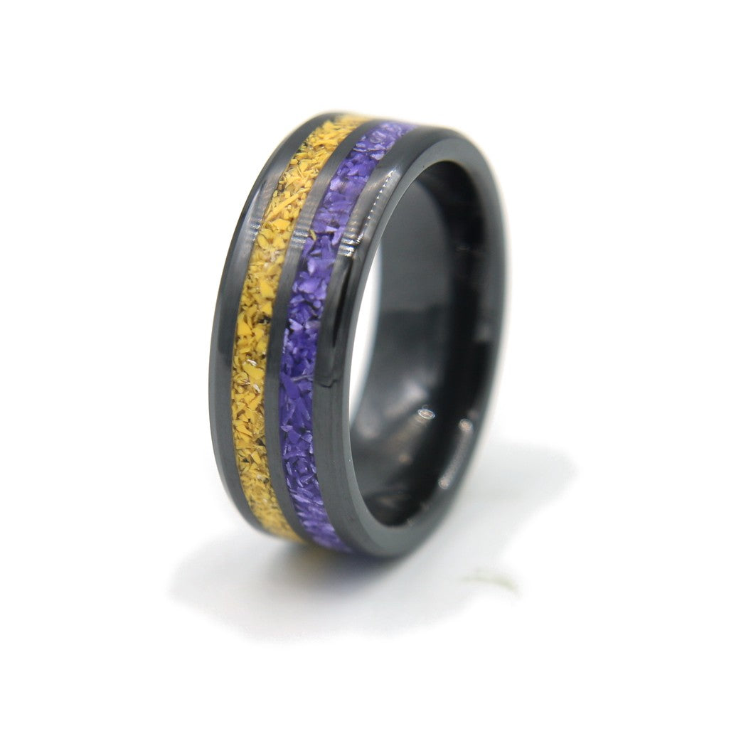 Black ceramic double-channel ring inlaid with purple and yellow Colorstone, standing on white