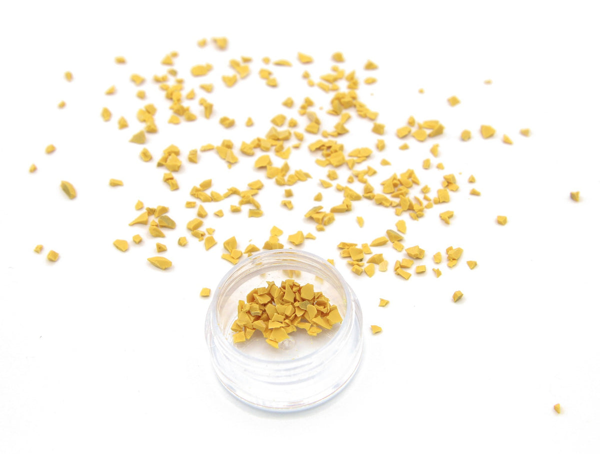 Yellow Colorstone fragments scattered on white, with a small jar of the crushed stone