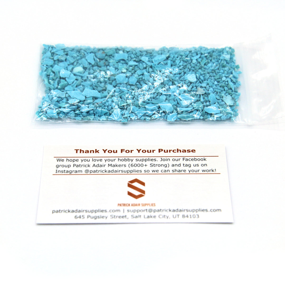 A 25 g bag of turquoise fragments next to our thank-you card, for scale